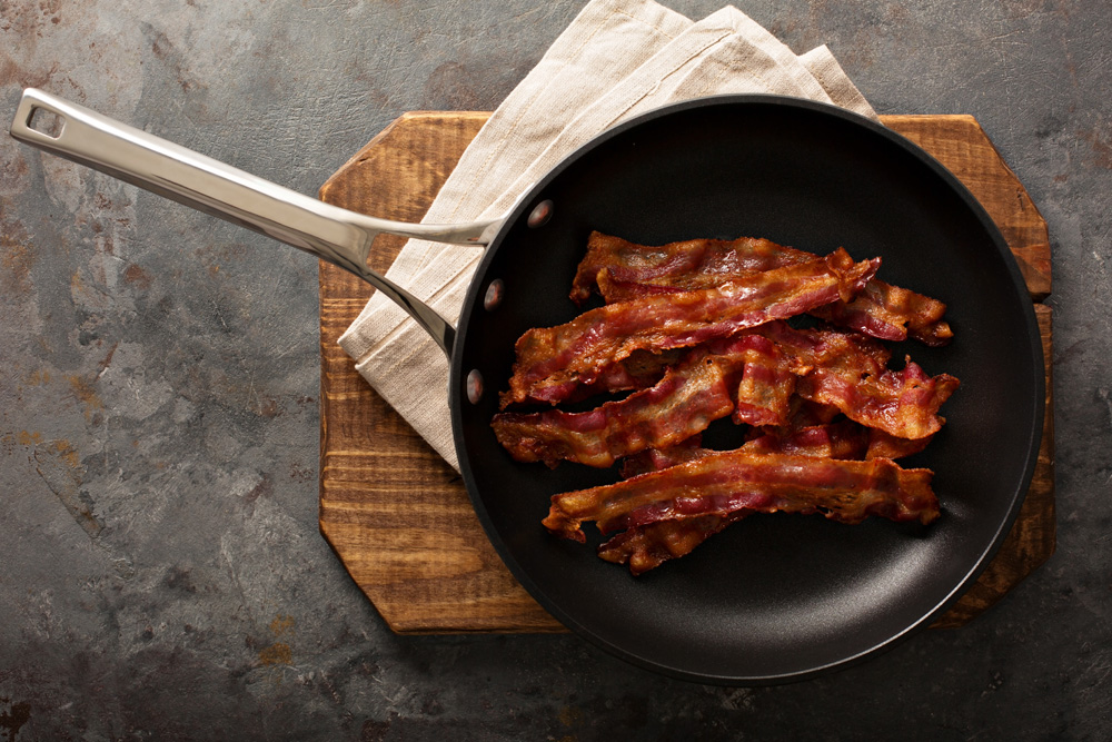 Picture of bacon sizzling in a cast iron pan on a wooden serving platter