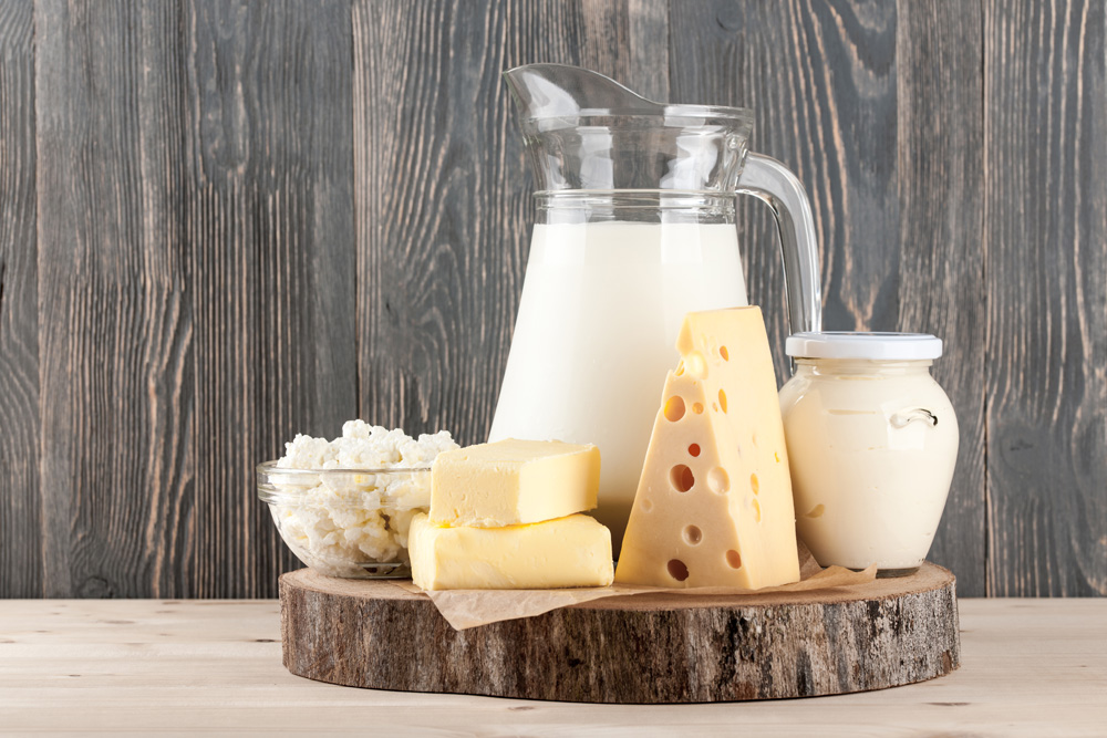 Photo of milk, cheese, butter, and yogurt arranged on a serving platter made of wood 