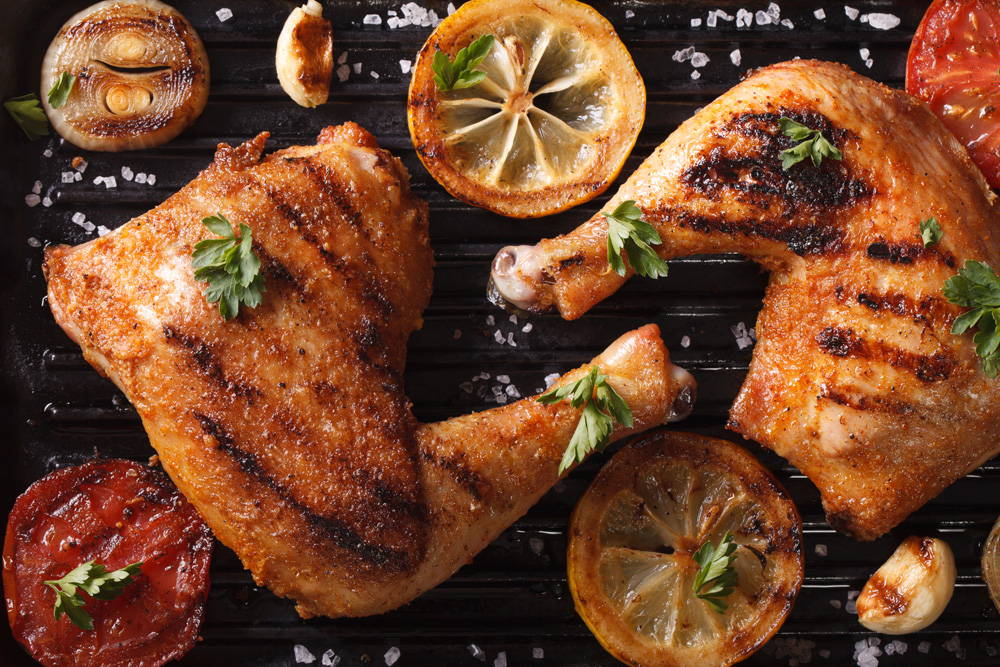Image of roasted chicken garnished with roasted lemons, tomatoes and onions on a platter