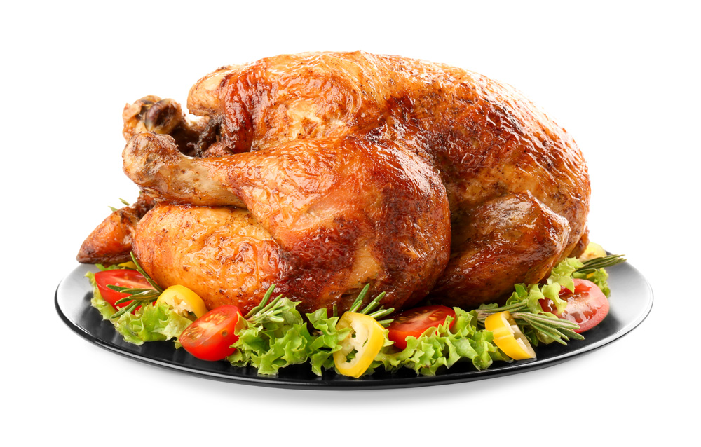 Photo of a whole roast turkey on a black ceramic plate garnished with greens, tomatoes and yellow peppers on a white background