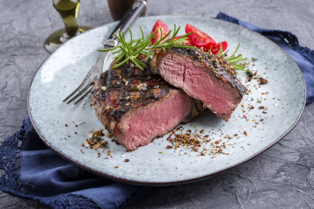 Photo of a bison steak cooked to medium rare and garnished with fresh rosemary served on a ceramic plate