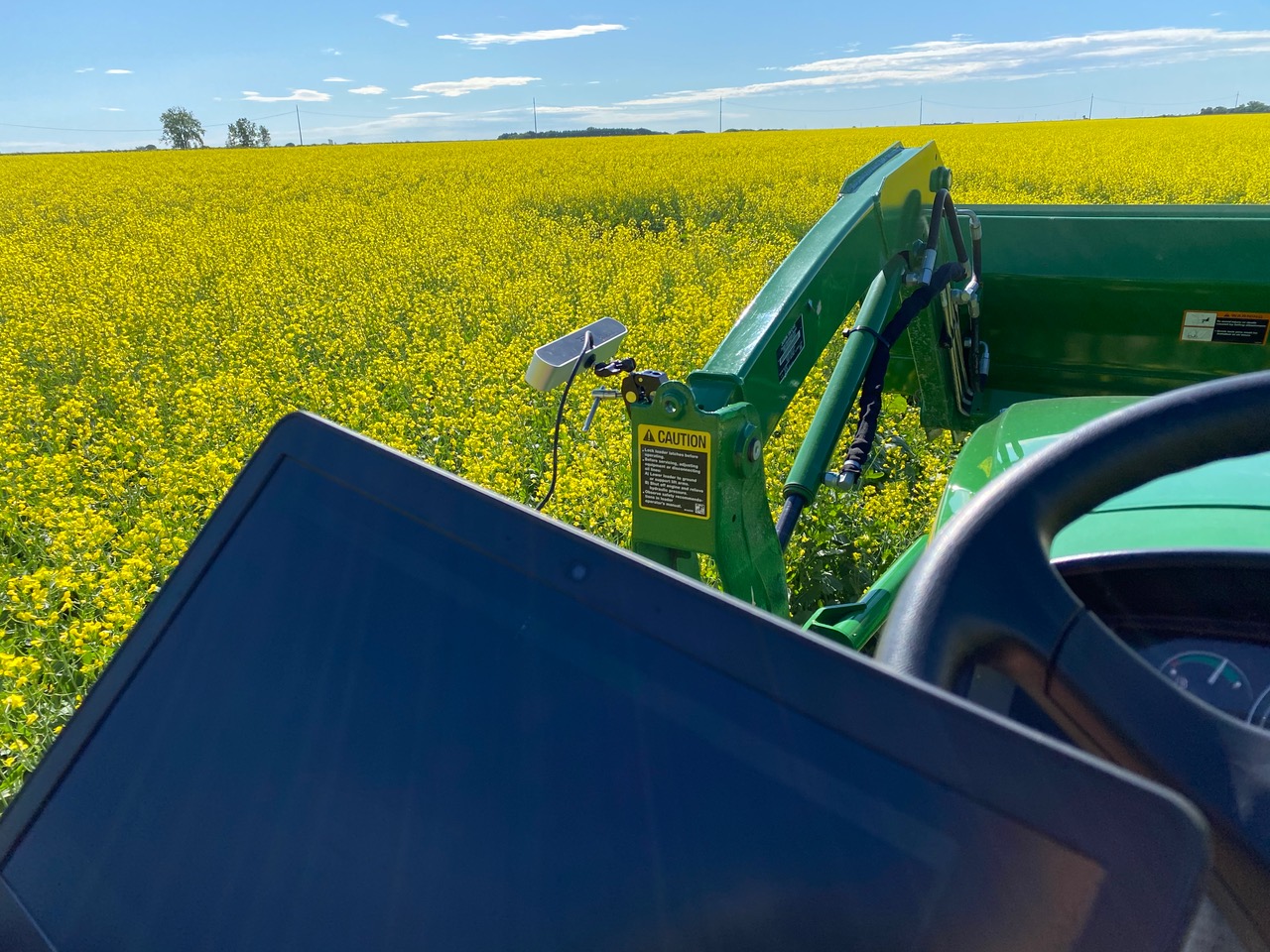 Photo from the perspective of a farmer on a tractor of a tablet being used to measure and monitor conditions in a canola field