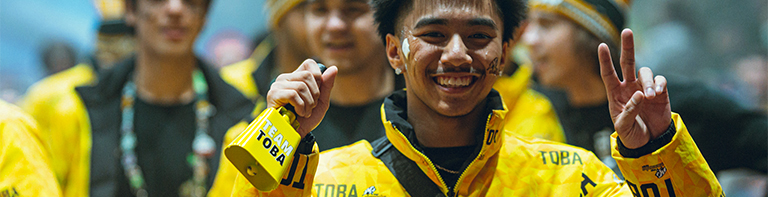 smiling athlete is giving the peace sign and holding a bell that is labelled Team Toba