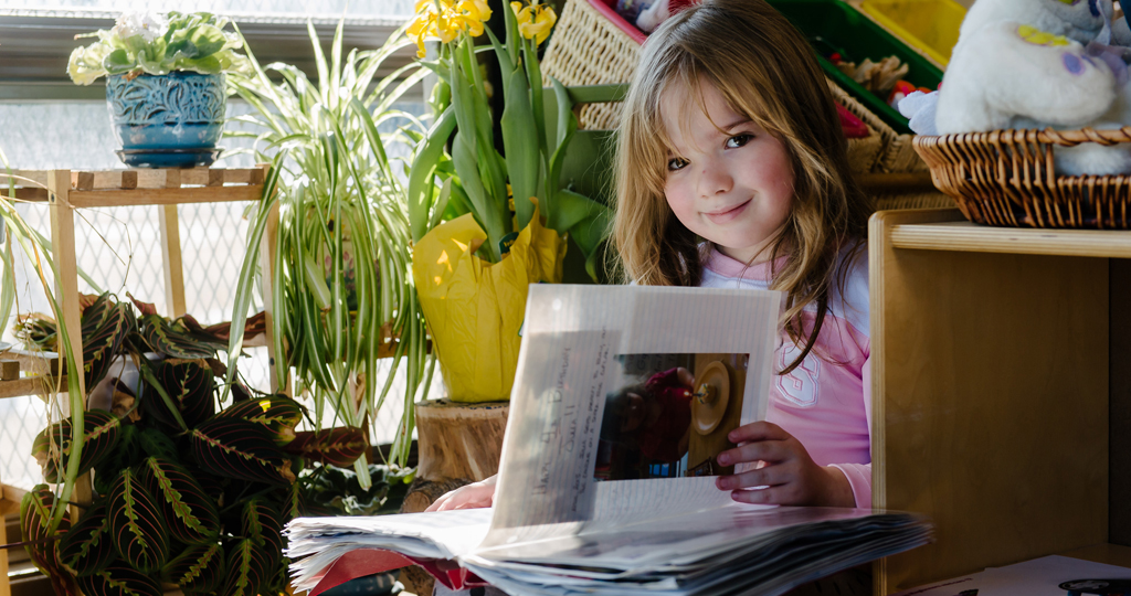 Young girl smiling and reading a book open on her lap