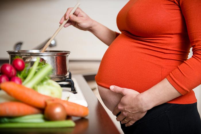 Image of a pregnant woman at a stove cooking