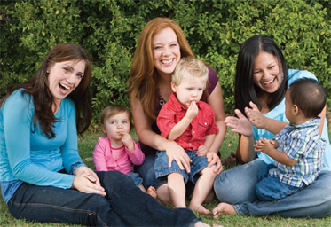 three woman playing and smiling with three toddlers on grass
