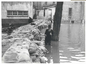 News anchor standing in waist deep water behind a sandbag dike while covering a story, 1950