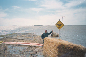Man standing before a flooded road pointing to a sign that states “IMPASSABLE WHEN WET”, 1997